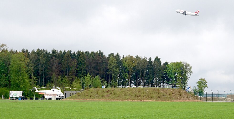 Der Spotterhügel von 2017 bis 2023, daneben der zum Grillstand umfunktionierte Helikopter Mil-Mi8, und über allem eine in den regnerischen Mittagshimmel startende Swiss-Maschine. 