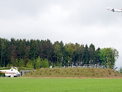 Der Spotterhügel von 2017 bis 2023, daneben der zum Grillstand umfunktionierte Helikopter Mil-Mi8, und über allem eine in den regnerischen Mittagshimmel startende Swiss-Maschine. 